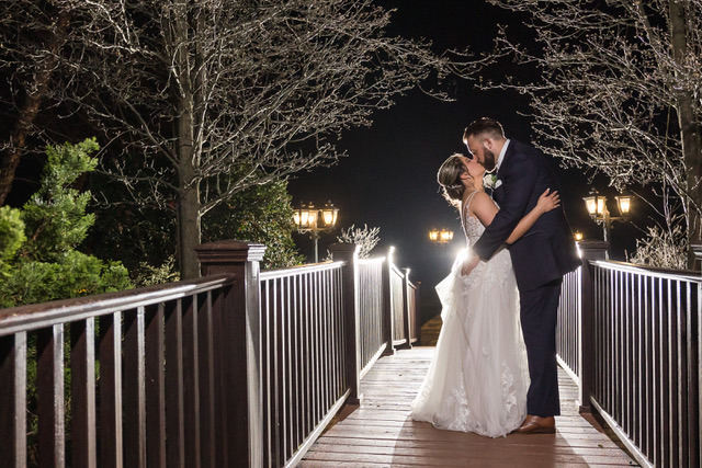 A bride and groom kiss outdoors on a bridge.